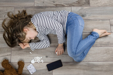 Sad cute Caucasian teenager girl, schoolgirl in depression lies on the floor, next to the phone, a...