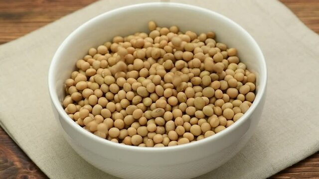 Dry raw soya beans falling into a white bowl, slow motion	