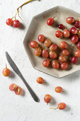 Pink grapes with water drops in a plate on delicate grey stone background. Top view. Copy space