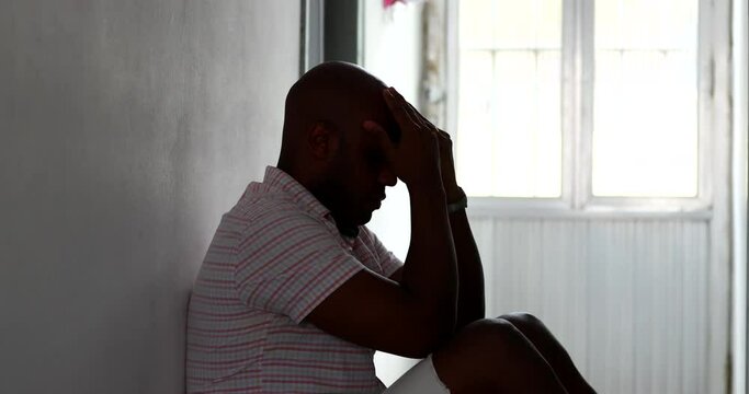 Desperate black African man sitting on home floor in despair and depression