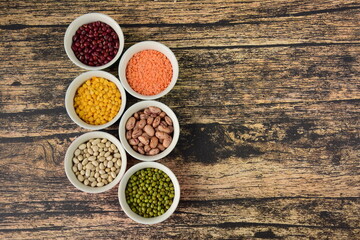 Assorted Legumes: borlotti beans, mung beans and red, yellow lentils variety on wooden background. Flat lay, negative space
