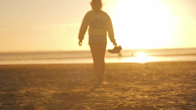Silhouette Of A Woman Walking Barefoot On The Beach On Sunset In Croyde Bay, North Devon, UK.  - wide shot