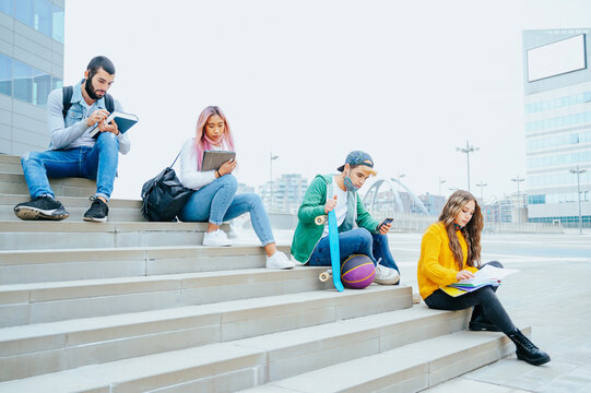 Group of multiracial students in protective masks study sitting on stairs in social distance outside a college
