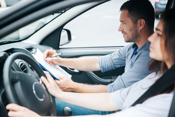 Satisfied male driving instructor notes results of test in his paper. Smiled man sitting on front...