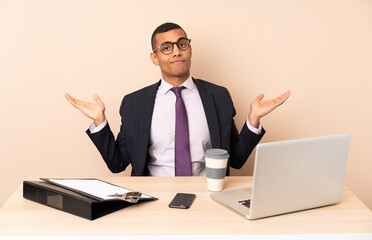 Young business man in his office with a laptop and other documents having doubts while raising hands