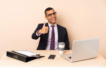 Young business man in his office with a laptop and other documents with thumbs up because something good has happened