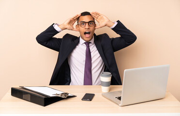 Young business man in his office with a laptop and other documents with surprise expression