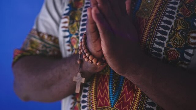 A Religious African Man in Traditional African Dress Solemnly Praying With Rosary Coiled Around His Hand. - Medium Shot