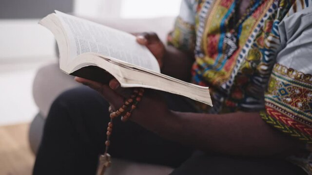 Cropped Image Of A Man Sitting While Holding And Reading Holy Bible With Rosary On His Hands. - Medium Shot