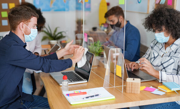 Coworking office with multiracial people wearing surgical face mask - Young man disinfect laptop with alcohol liquid - Powered by Adobe