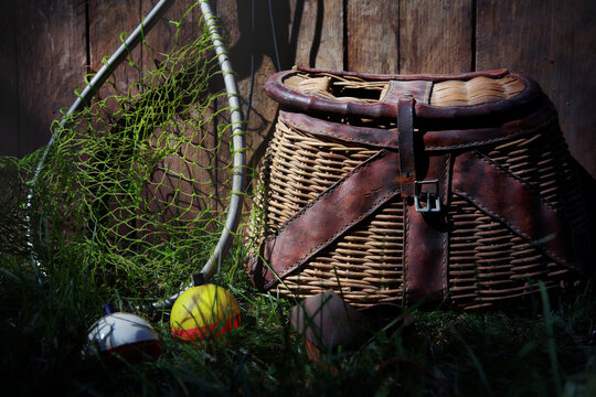 Fishing bobbers and net with vintage Creel basket against a wooden fence