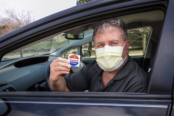 Man holding an "I voted today" sticker after voting wearing a face mask to prevent the spread of coronavirus