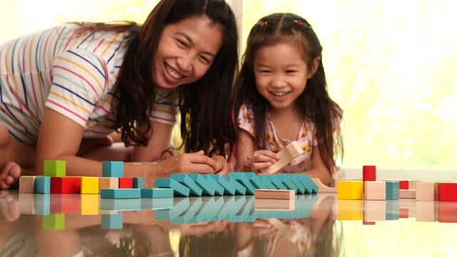 Happy family young mother and dauther playing colorful wooden building blocks. Concept of friendship and learn through playing activity, funny educational games for children development.
