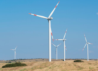 Wind turbines on beautiful sunny summer autumn of the hills of Apuliia (murgia). Curvy road through Eolic park. Green ecological power energy generation. Wind farm eco field