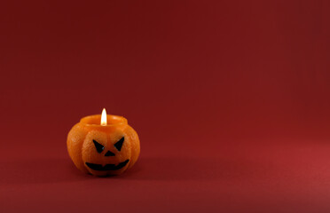 One scary orange pumpkin shaped candle with a fire, isolated on red background, space for text. Tradition Happy Halloween concept. Dark tones picture