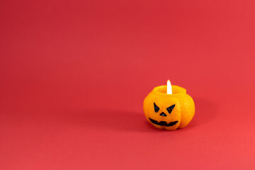 One scary orange pumpkin shaped candle with a fire, isolated on red background, space for text. Tradition Happy Halloween concept.