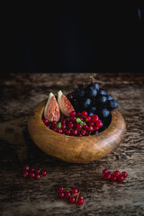 Fig, grape, red currant in a wooden bowl on a dark background.