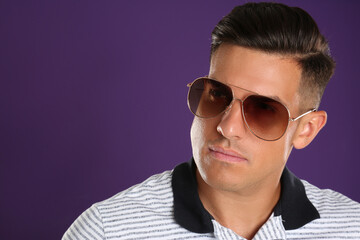 Obraz premium Handsome man wearing sunglasses on purple background, closeup. Space for text