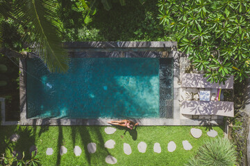 Beautiful girl relaxing outdoor in her garden with swimming pool. Summer concept about lifestyle,beauty, vacations and real estates. Aerial drone view