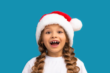 A little girl in a Christmas hat poses on a blue background.