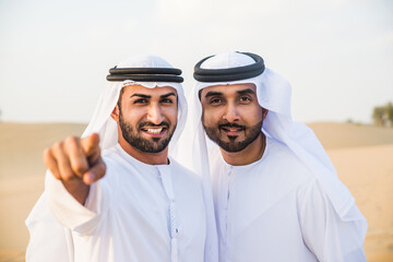Fototapeta premium Two business men wearing traditional uae white kandura spending time in the desert of Dubai