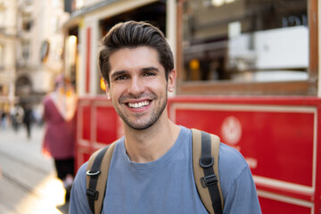 Portrait of a young handsome tourist man with a wide beautiful smile near the historic red tram on...