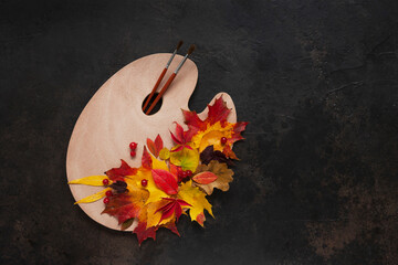Artist Autumn. Multi-colored fallen leaves from trees on a palette and brushes on dark background....