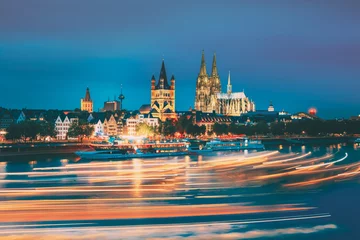 Köln, Deutschland. Große St.-Martin-Kirche und Dom in Köln am Abend mit Reflexion im Rhein. Blaue Stunde am Abend. Lichtspuren auf dem Wasser von Sportbooten in Langzeitbelichtungsfotografie. © Great Brut Here