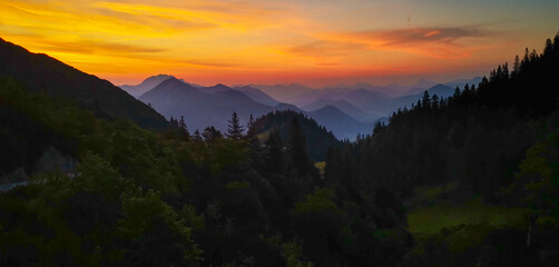 Scenic sunrise in the bavarian alps with dark green forest in the foreground