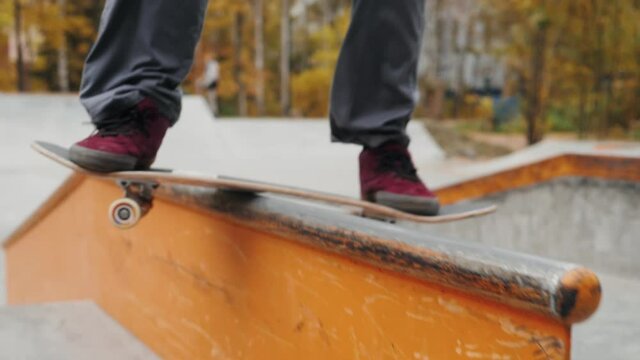 Skater practicing in the autumn concrete skate park, making tricks and rides in ramp. Skateboarder making tricks, manual balance, boardslide and stalls, professional extreme sport
