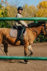 Happy little ginger girl riding on a small brown horse. Holding reins.