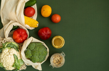 Vegetables in eco bag and nuts in a glass jar on green surface. Pepper, tomato, corn, cucumber, broccoli, cauliflower in reusable shopping eco friendly cotton fabric bags. Zero waste plastic free.