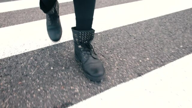 Steps on the road. Close-up of feet in black boots walk along a white stripes of a pedestrian crossing in the city. Zebra crossing accident claims. 