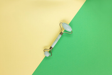 Green Gua Sha facial massage tools. Green Quartz jade roller on yellow background. Anti age, lifting and toning treatment at home.