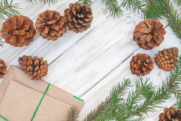 christmas background. pine cones, spruce branches and paper envelopes on a white wooden background with an empty space in the center