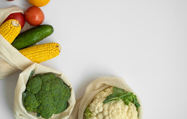 Vegetables in eco bag on white surface with a copy space. Pepper, tomato, corn, cucumber, broccoli, cauliflower in reusable shopping eco friendly cotton fabric bags. Zero waste plastic free concept.