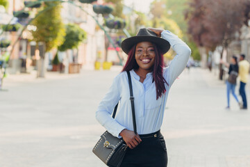 smiling young African American girl with pink hair wearing a hat walking down the street on a sunny day.