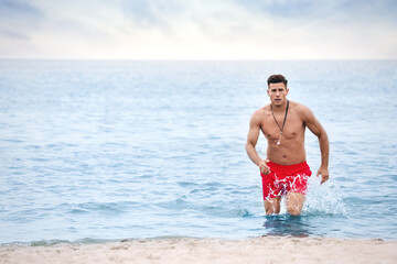 Fototapeta na wymiar Handsome male lifeguard running on sandy beach
