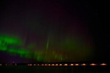 A tranquil view of Aurora borealis green beam of northern lights with purple tail beside a lake under starry sky