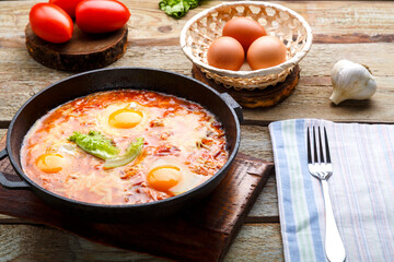 israeli fried eggs shakshuka with cheese in a frying pan next to a fork and a napkin.