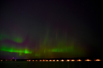 Dark night Green Aurora borealis lights with purple tail beside a lake under starry sky with reflection in scandenavia