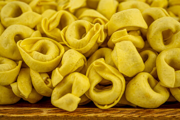 Italian uncooked pasta Tortellini with cheese on a wooden plate. Traditional Italian food. Selective focus.