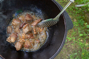 Cooking pilaf in a cauldron on the grill outside in the summer