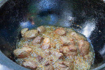 Cooking pilaf in a cauldron on the grill outside in the summer