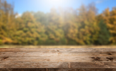 Naklejka na ściany i meble Autumn background, empty old rustic wood table with blur forest trees and sunlight, Autumn fall backdrop, banner for product display copy space, thanksgiving concept rustic textured grungy floor.