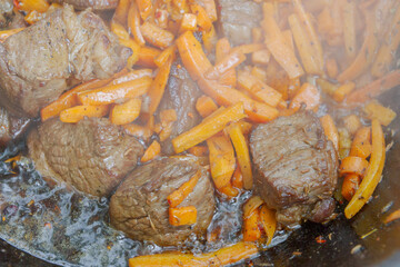 Cooking pilaf in a cauldron on the grill outside in the summer