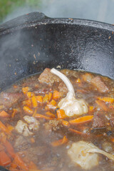 Cooking pilaf in a cauldron on the grill outside in the summer