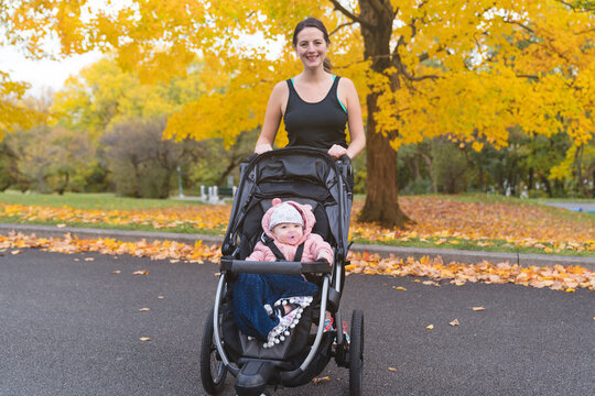 Beautiful young mother with her daughter in jogging stroller outside in autumn nature