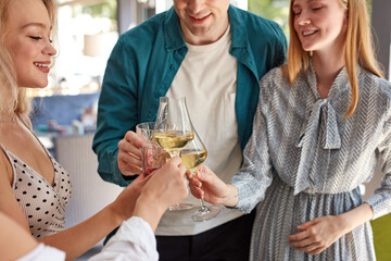 friends clinking glasses above dinner table in restaurant, hands of people with glasses. celebrating and toasting in honor of the wedding or other celebration, in cafe