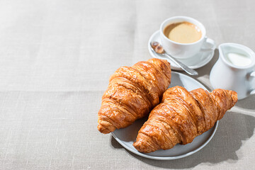 Croissants and cup of coffee in the morning light, sunlight shadow, on a linen fabric. Morning breakfast concept.